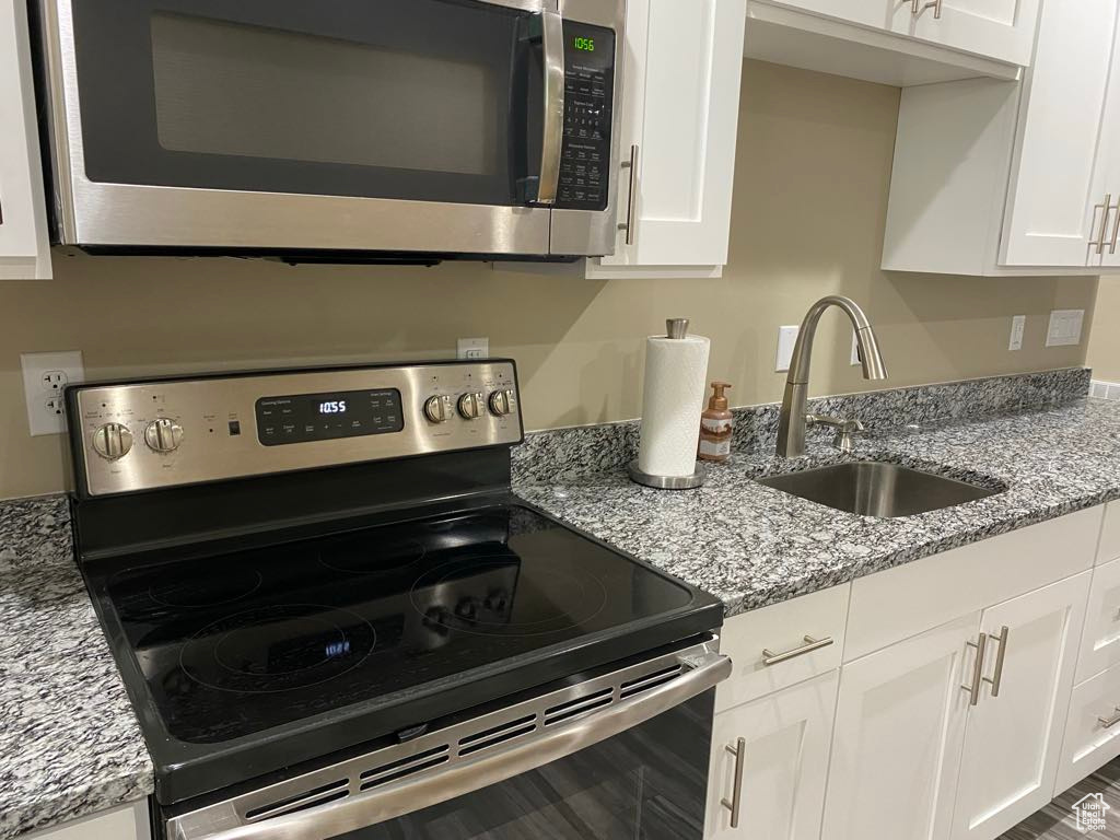 Kitchen featuring white cabinets, light stone countertops, appliances with stainless steel finishes, and a sink