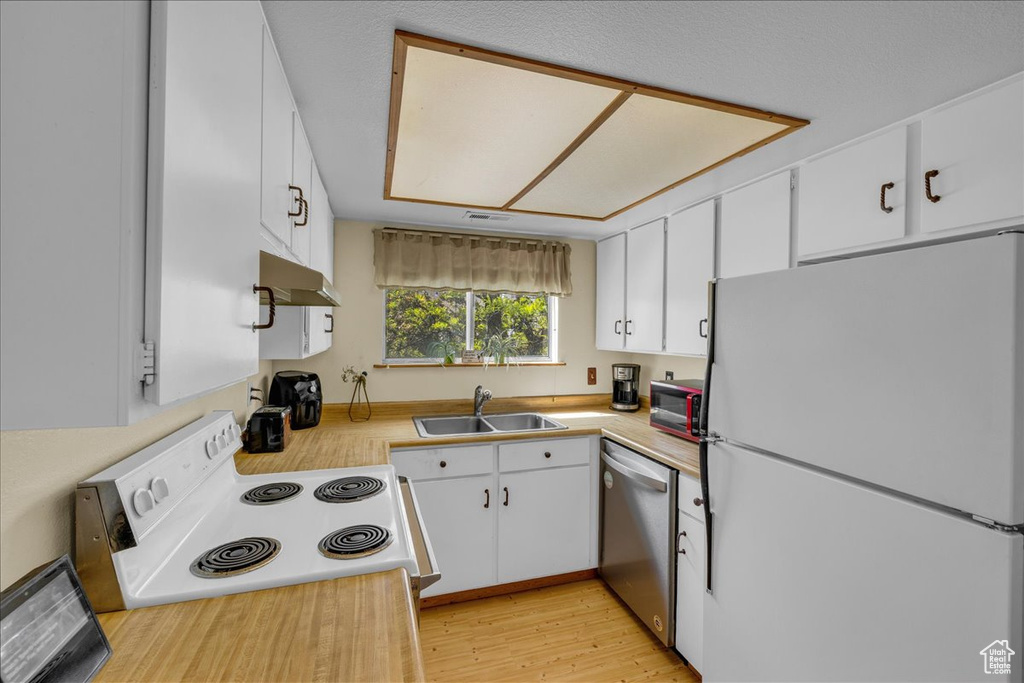 Kitchen with a sink, light countertops, light wood finished floors, under cabinet range hood, and white appliances