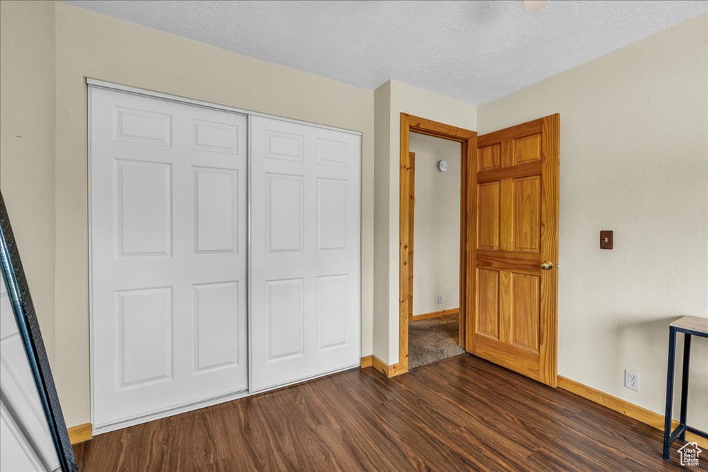 Unfurnished bedroom with baseboards, a textured ceiling, dark wood finished floors, and a closet