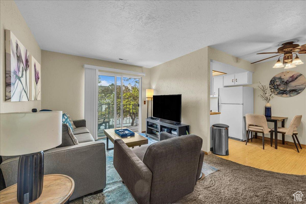 Living area with a textured ceiling, visible vents, ceiling fan, and wood finished floors