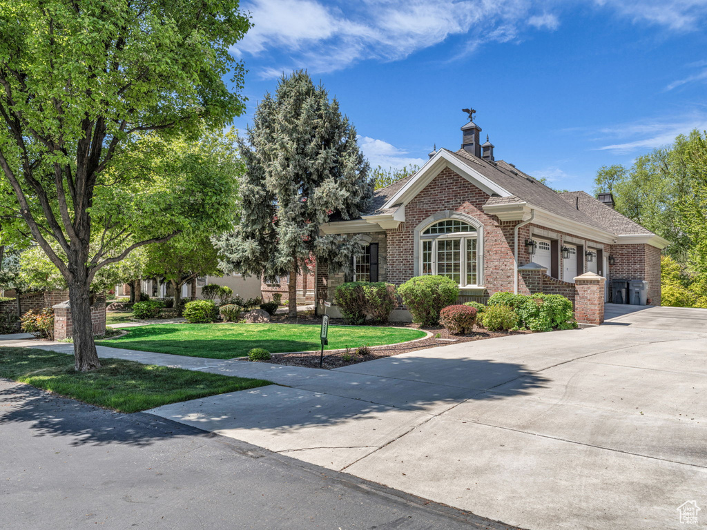 View of front of house with a garage, a front lawn, a chimney, brick siding, and driveway