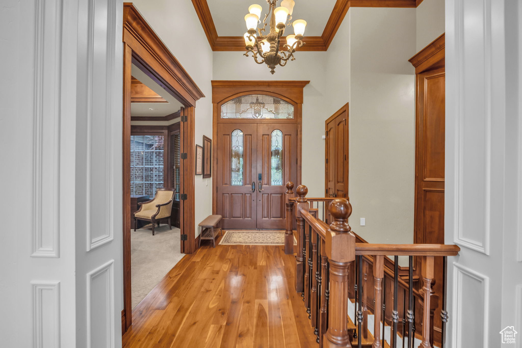 Foyer entrance with crown molding, an inviting chandelier, and light wood-type flooring