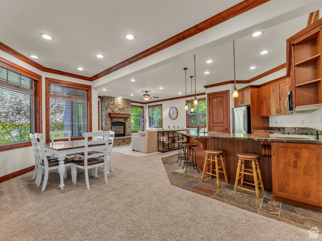 Carpeted dining room with ornamental molding, a fireplace, baseboards, ceiling fan, and recessed lighting
