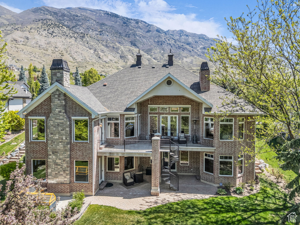 Back of property featuring a patio, a chimney, brick siding, a mountain view, and a yard