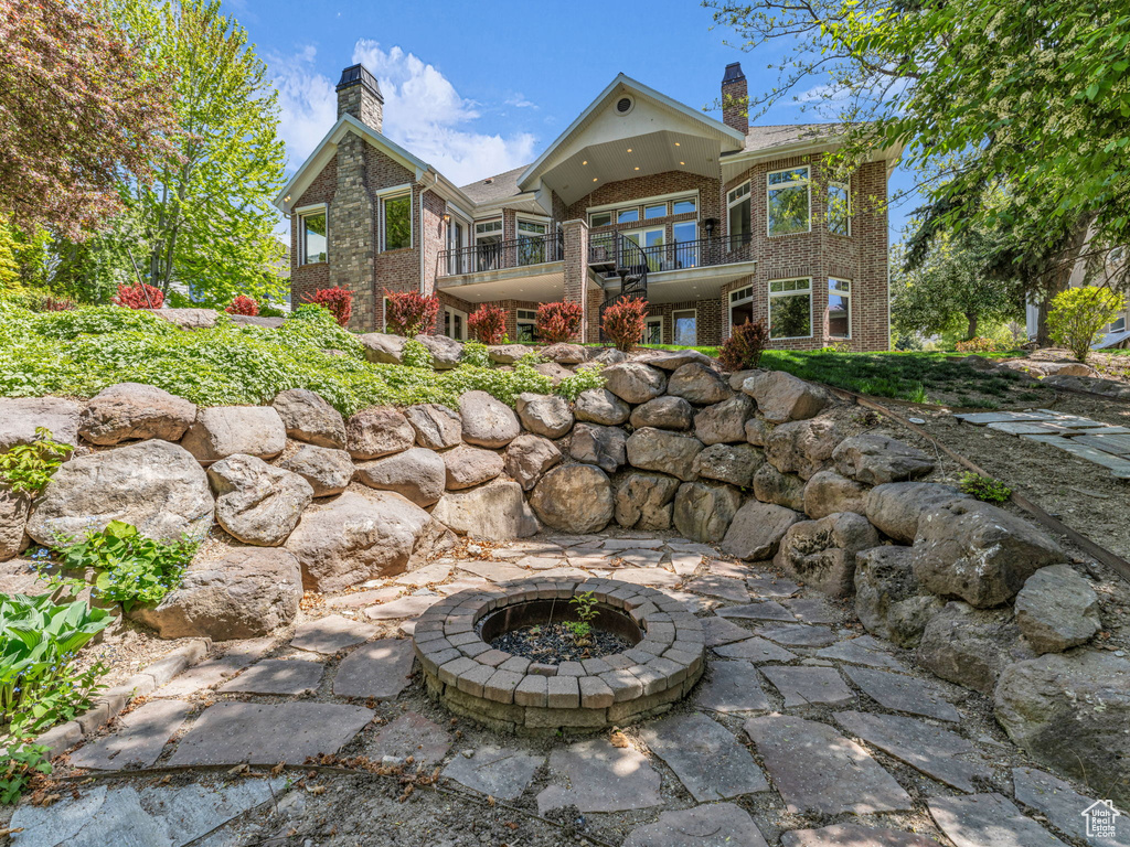 Rear view of house featuring a chimney, a fire pit, brick siding, and a balcony