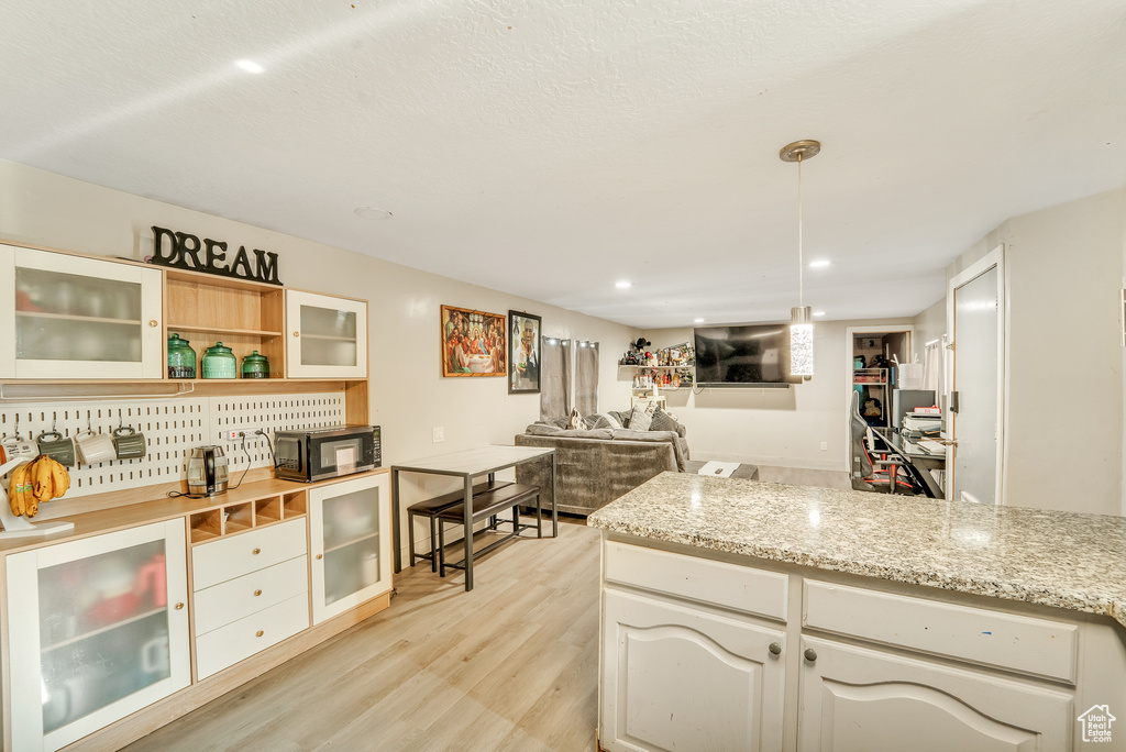 Kitchen featuring light wood-style floors, open shelves, black microwave, and glass insert cabinets