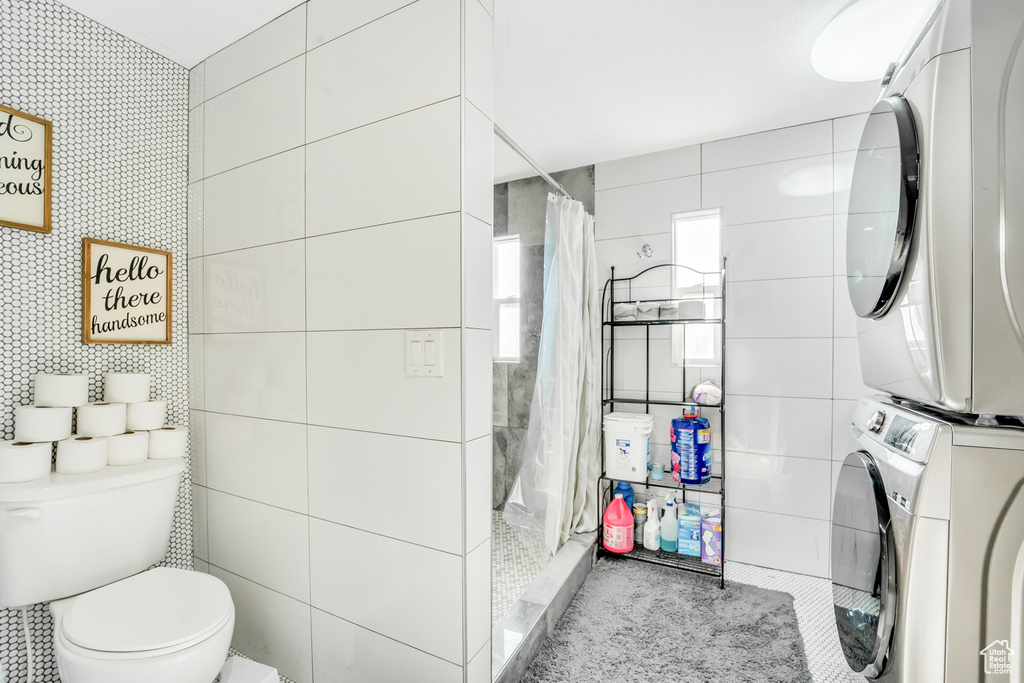 Bathroom featuring stacked washer and dryer, a shower with curtain, tile walls, and toilet