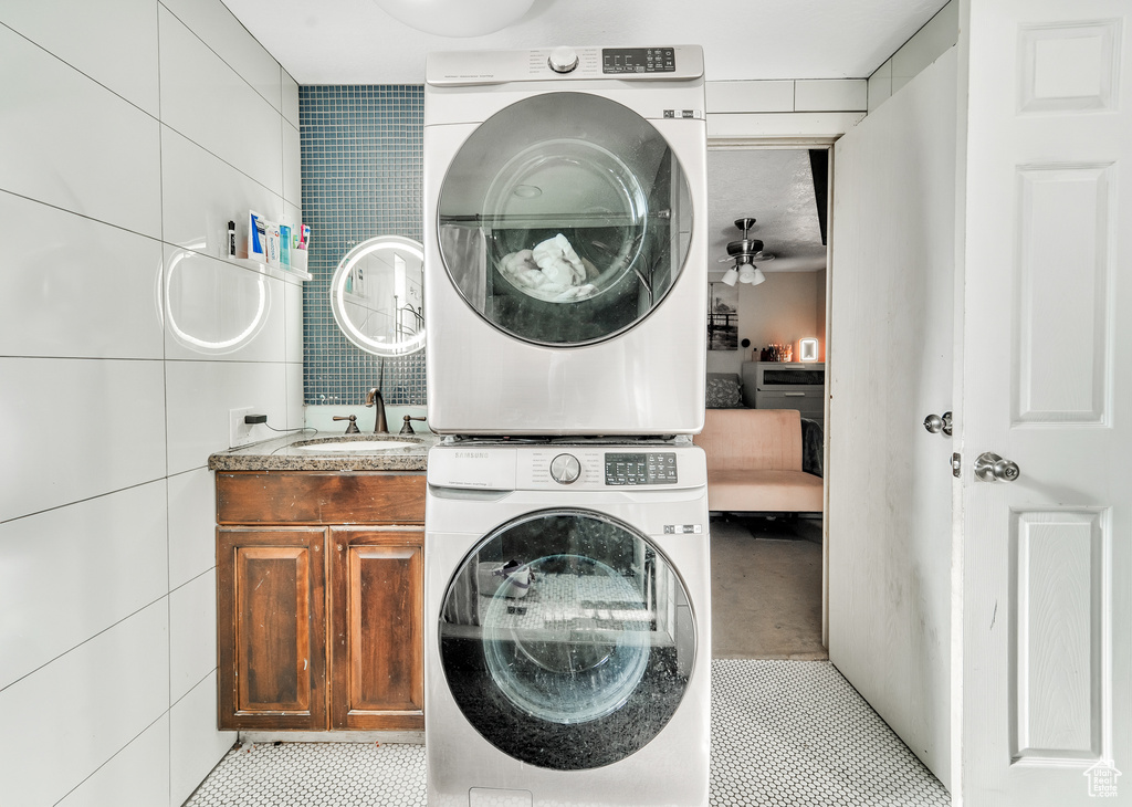 Clothes washing area featuring tile walls, stacked washer / drying machine, cabinet space, a sink, and light tile patterned flooring