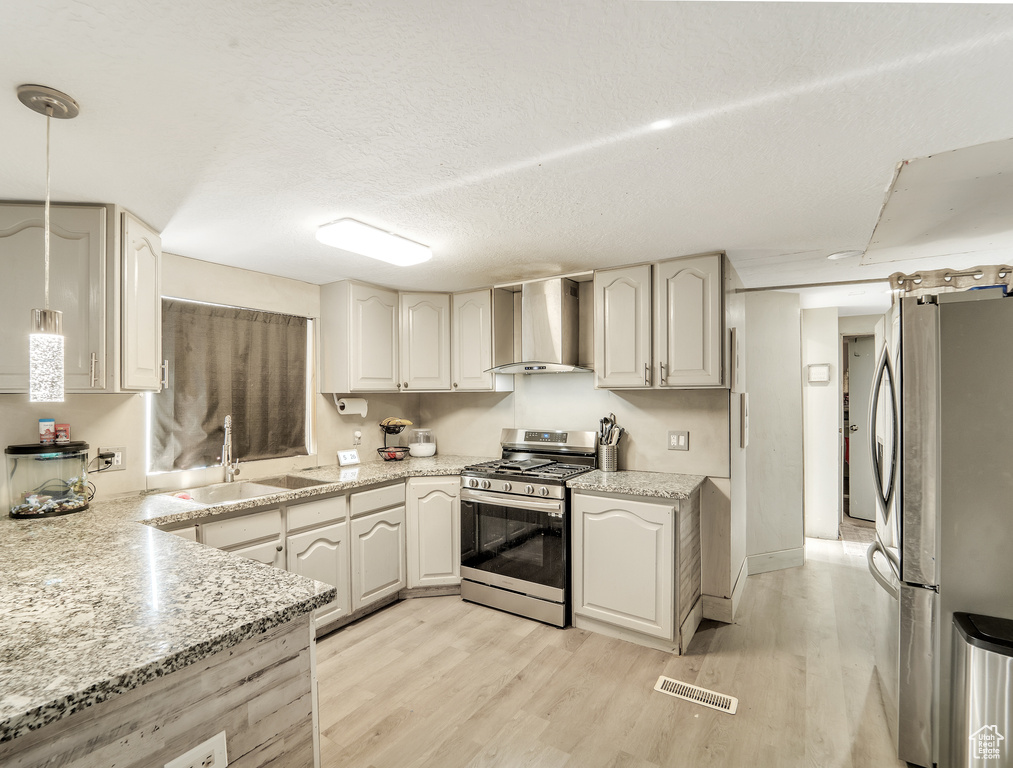 Kitchen featuring wall chimney range hood, appliances with stainless steel finishes, a sink, light wood finished floors, and visible vents