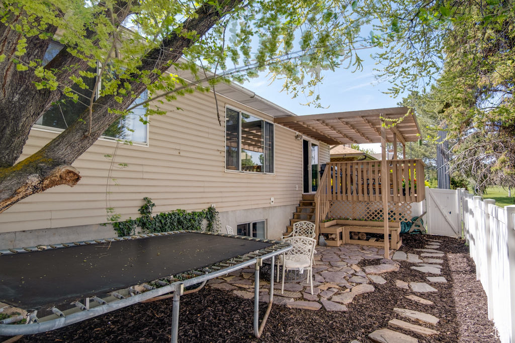 View of side of home featuring a trampoline, a wooden deck, a patio area, a fenced backyard, and a pergola