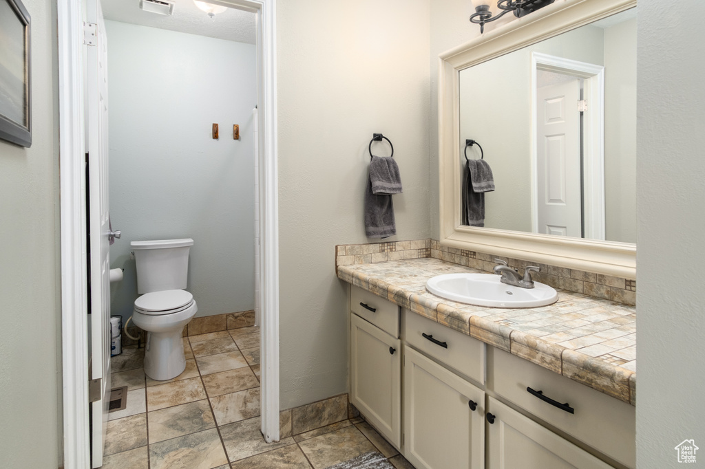 Bathroom with vanity, stone finish flooring, visible vents, and toilet