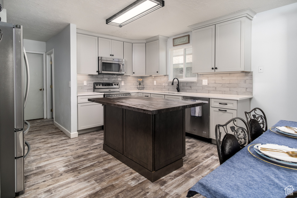 Kitchen with a sink, wooden counters, stainless steel appliances, wood finished floors, and tasteful backsplash