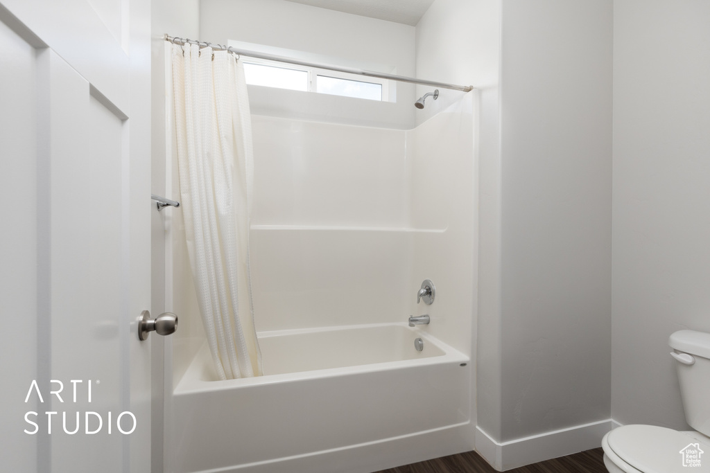 Full bath featuring baseboards, shower / tub combo with curtain, wood finished floors, and toilet