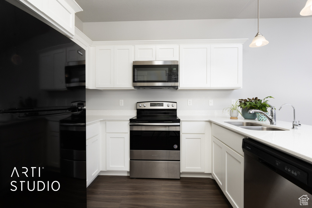 Kitchen with white cabinets, a sink, light countertops, stainless steel appliances, and dark wood-type flooring