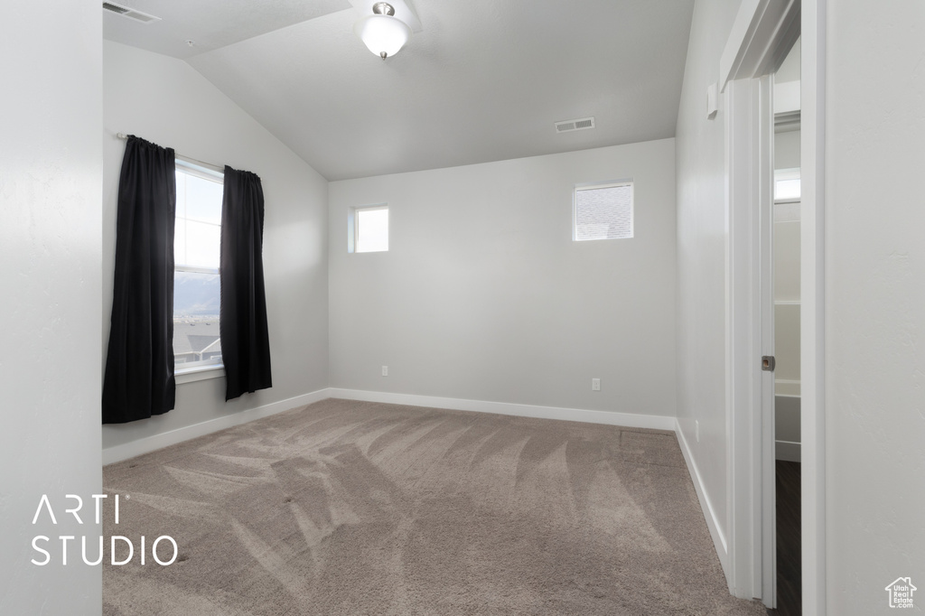 Carpeted spare room featuring visible vents, baseboards, and vaulted ceiling