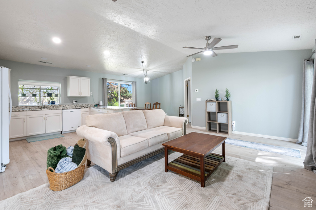 Living room with a textured ceiling, light wood-style flooring, ceiling fan, and a wealth of natural light