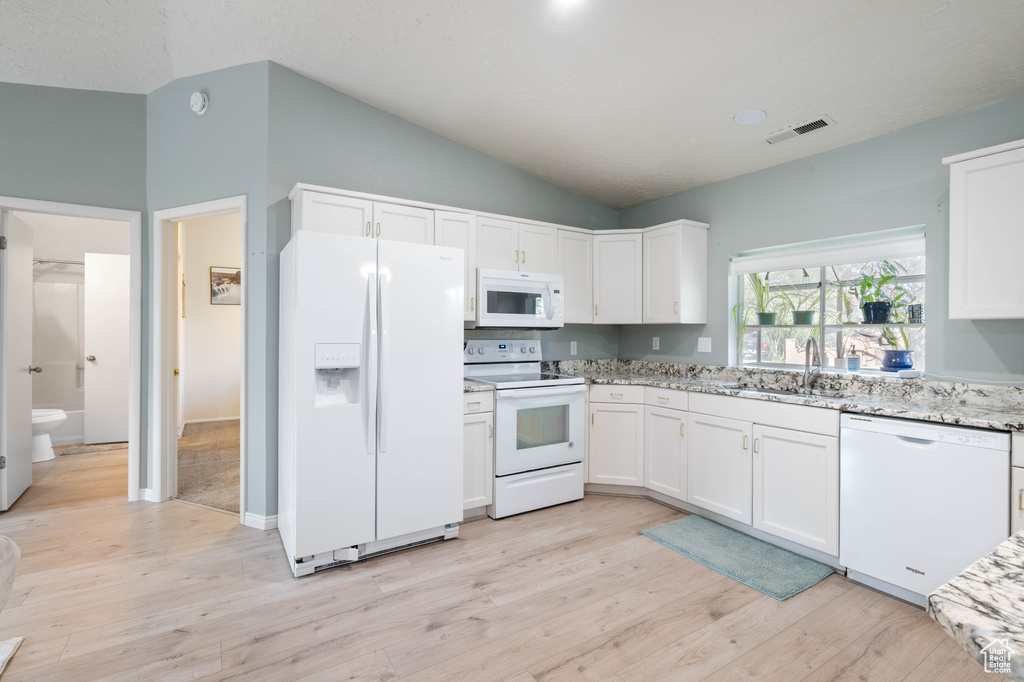 Kitchen with visible vents, vaulted ceiling, a sink, white cabinets, and white appliances
