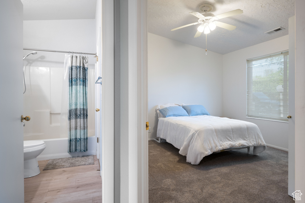 Bedroom with a textured ceiling, a ceiling fan, baseboards, wood finished floors, and visible vents