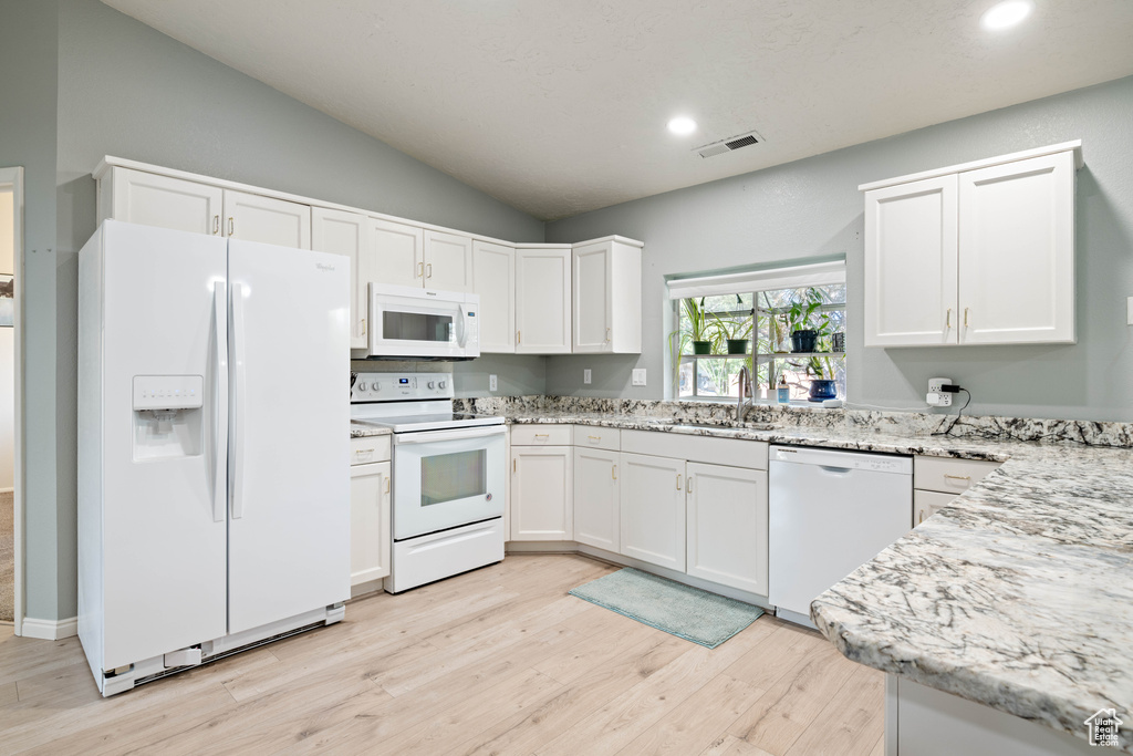 Kitchen with visible vents, white appliances, light wood-style floors, white cabinets, and vaulted ceiling