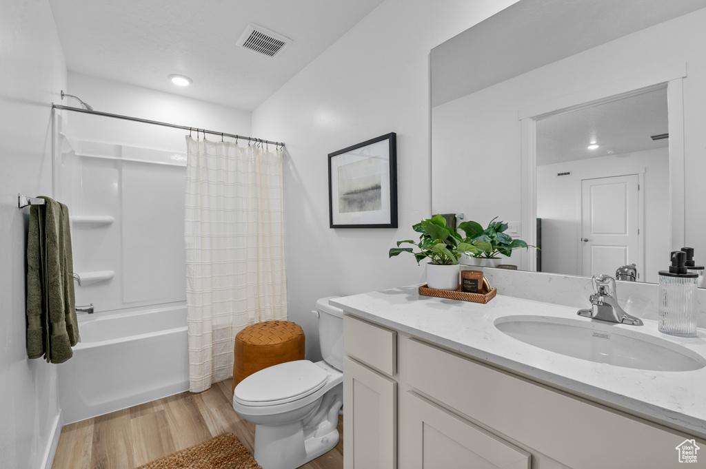 Bathroom with vanity, toilet, shower / bath combo with shower curtain, wood finished floors, and visible vents