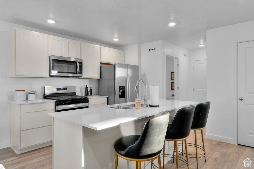 Kitchen featuring light wood-style floors, stainless steel appliances, a kitchen bar, and a sink