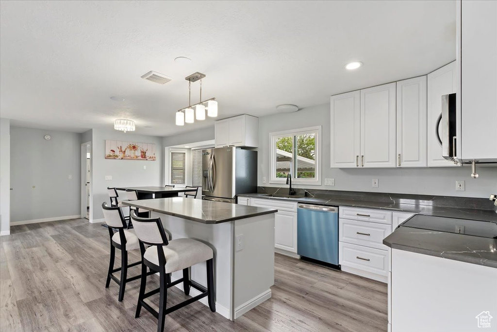 Kitchen with a sink, appliances with stainless steel finishes, a kitchen island, and dark countertops