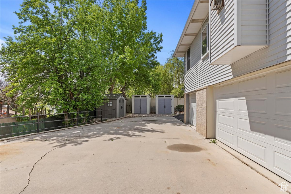 View of property exterior with a storage shed, driveway, fence, and an outdoor structure
