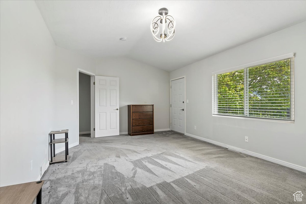 Unfurnished room with baseboards, a chandelier, vaulted ceiling, and light carpet