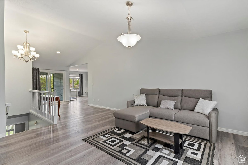 Living room with baseboards, wood finished floors, a chandelier, and vaulted ceiling