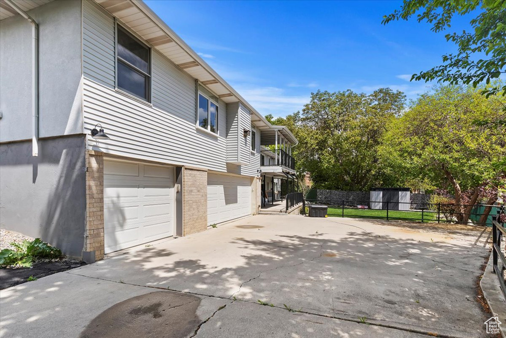 View of home\\\'s exterior featuring fence, a balcony, brick siding, an attached garage, and driveway