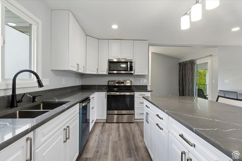 Kitchen featuring stainless steel appliances, white cabinetry, a sink, and light wood-style floors
