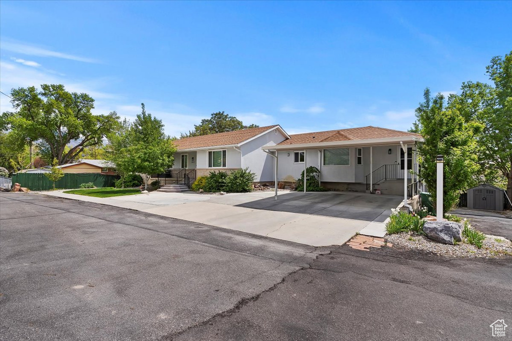 Ranch-style house with driveway, an outbuilding, fence, a shed, and stucco siding