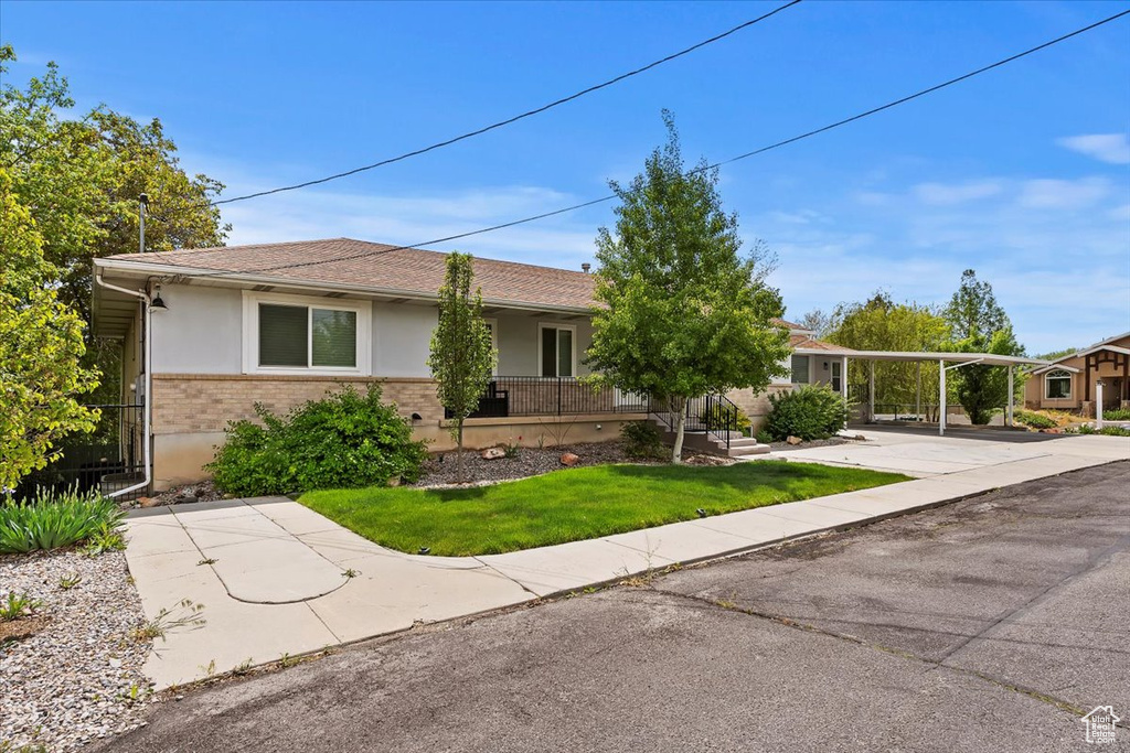 Ranch-style home with a shingled roof, brick siding, stucco siding, a front yard, and a carport