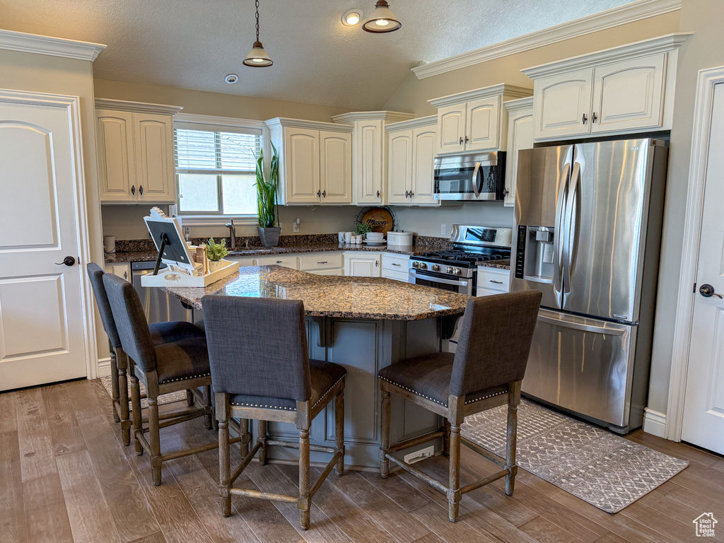 Kitchen featuring wood finished floors, a kitchen island, a kitchen bar, vaulted ceiling, and stainless steel appliances