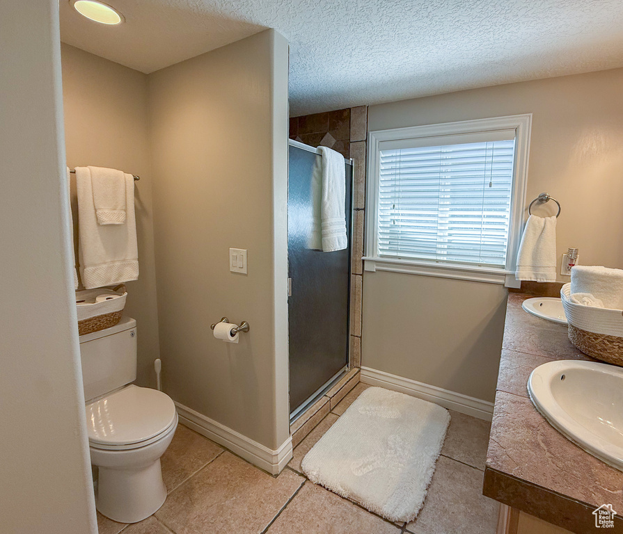 Bathroom featuring a sink, tile patterned flooring, double vanity, toilet, and a stall shower