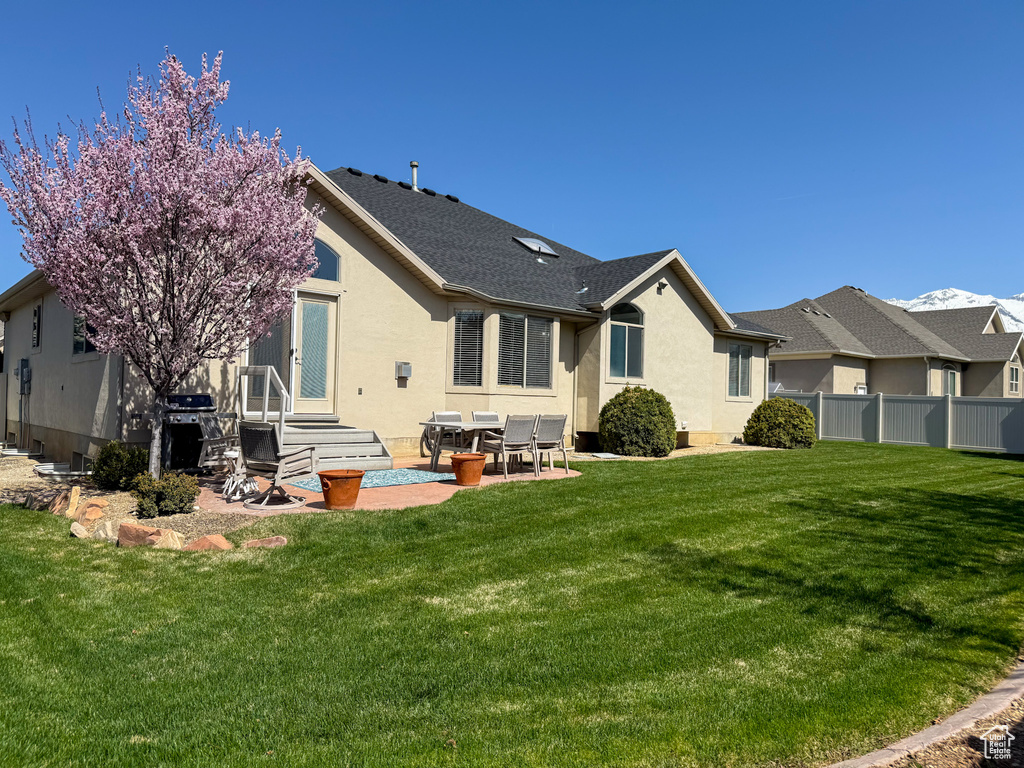 Back of property featuring fence, roof with shingles, stucco siding, a patio area, and a lawn