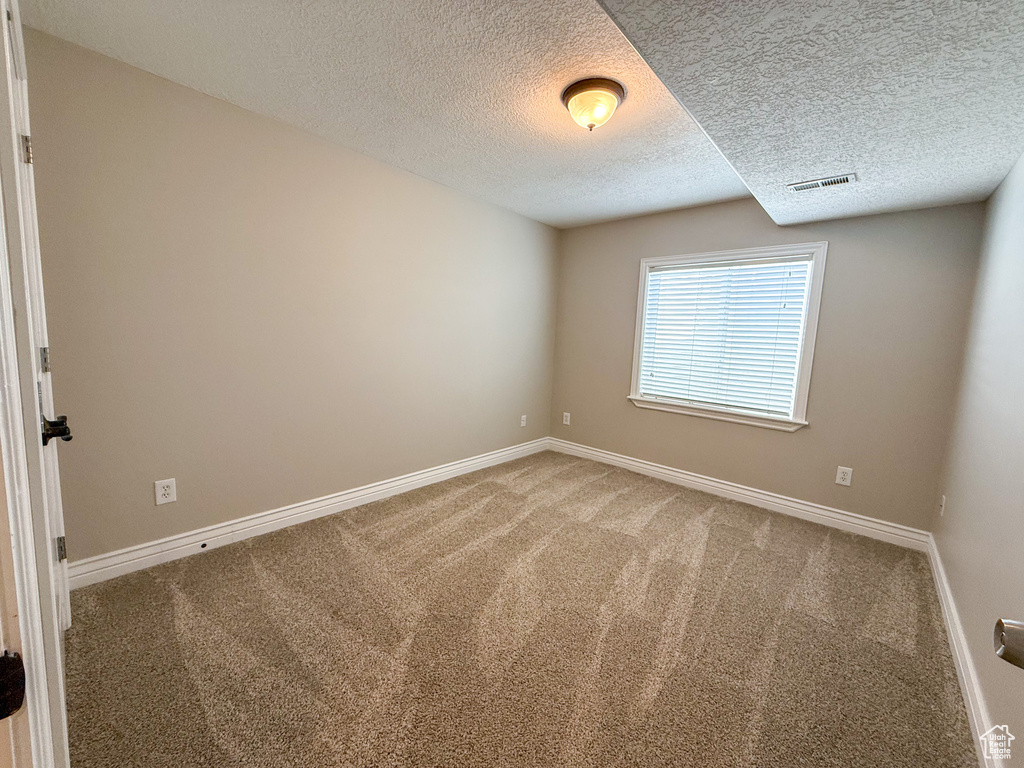 Carpeted spare room with a textured ceiling, baseboards, and visible vents