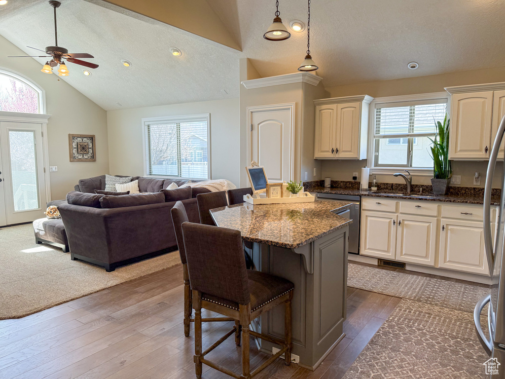 Kitchen with lofted ceiling, a kitchen island, a breakfast bar, ceiling fan, and stainless steel appliances