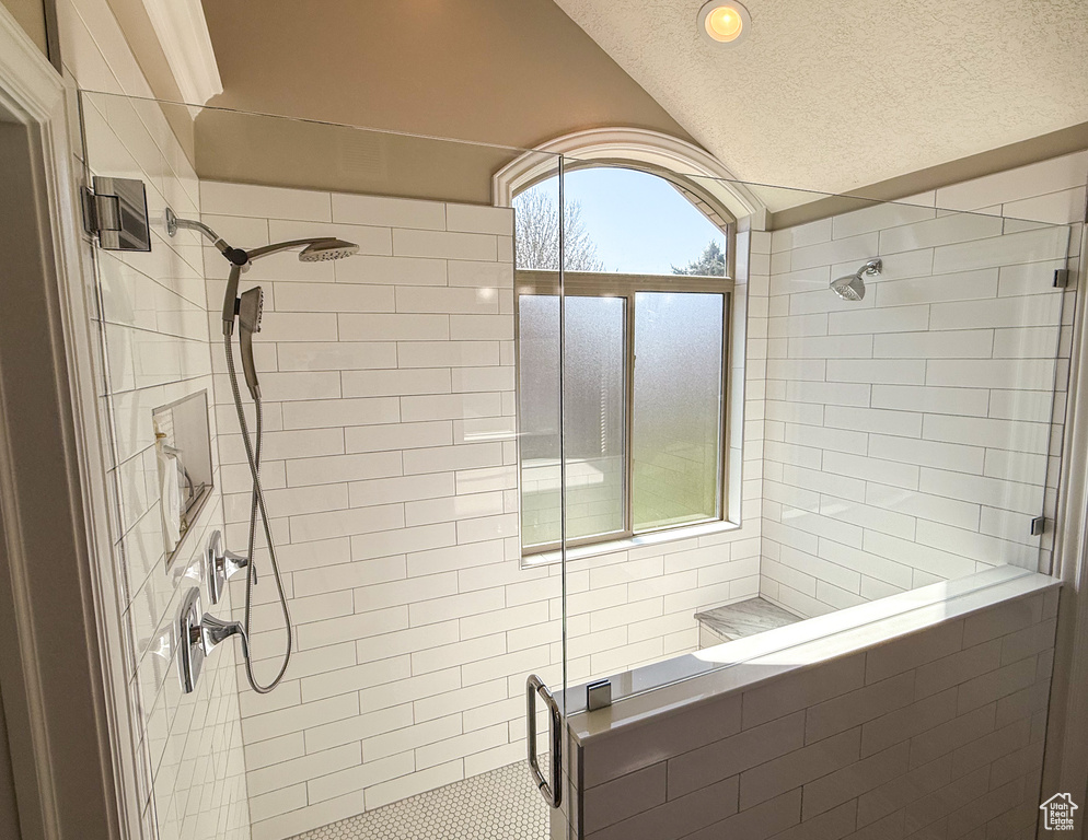 Full bath with a stall shower, a textured ceiling, and lofted ceiling