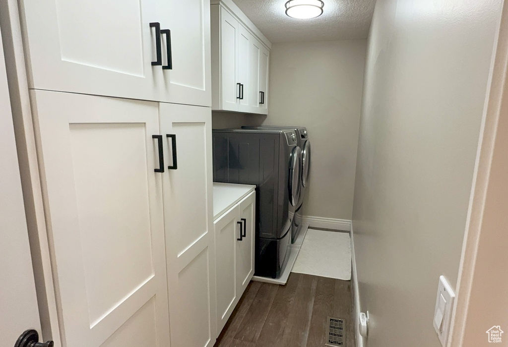 Clothes washing area with dark wood-style flooring, baseboards, washer and clothes dryer, a textured ceiling, and cabinet space