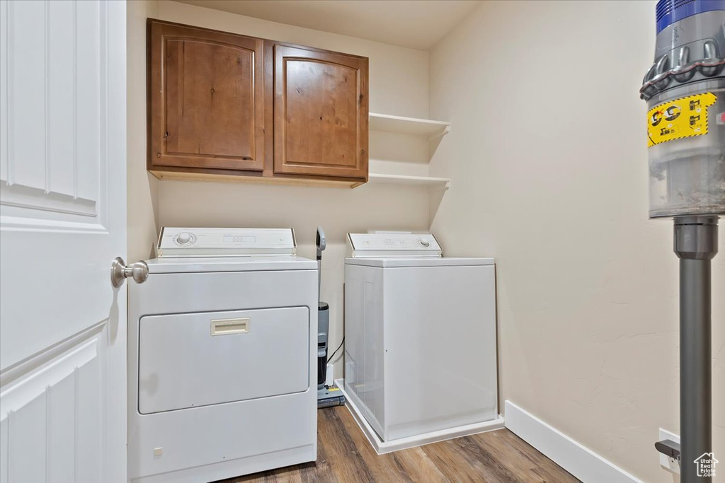 Clothes washing area featuring baseboards, cabinet space, wood finished floors, and washer and dryer