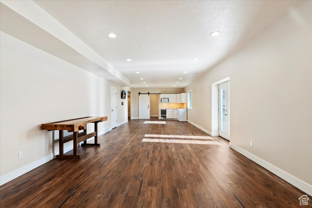 Unfurnished living room featuring baseboards, dark wood-style flooring, recessed lighting, and a barn door