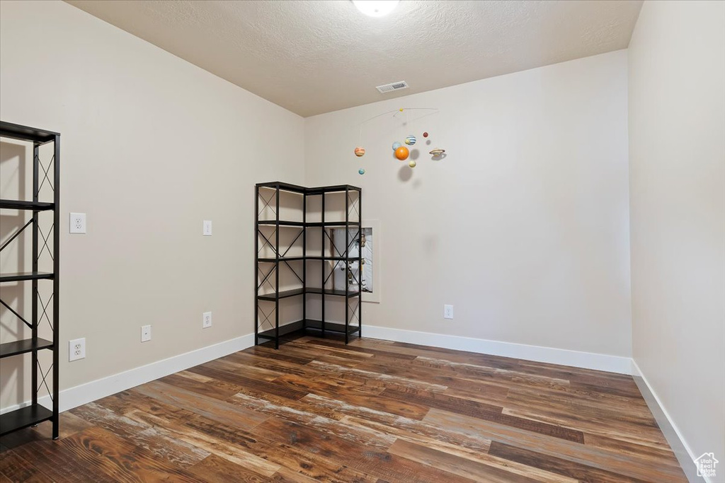Empty room with baseboards, dark wood-style floors, a textured ceiling, and visible vents