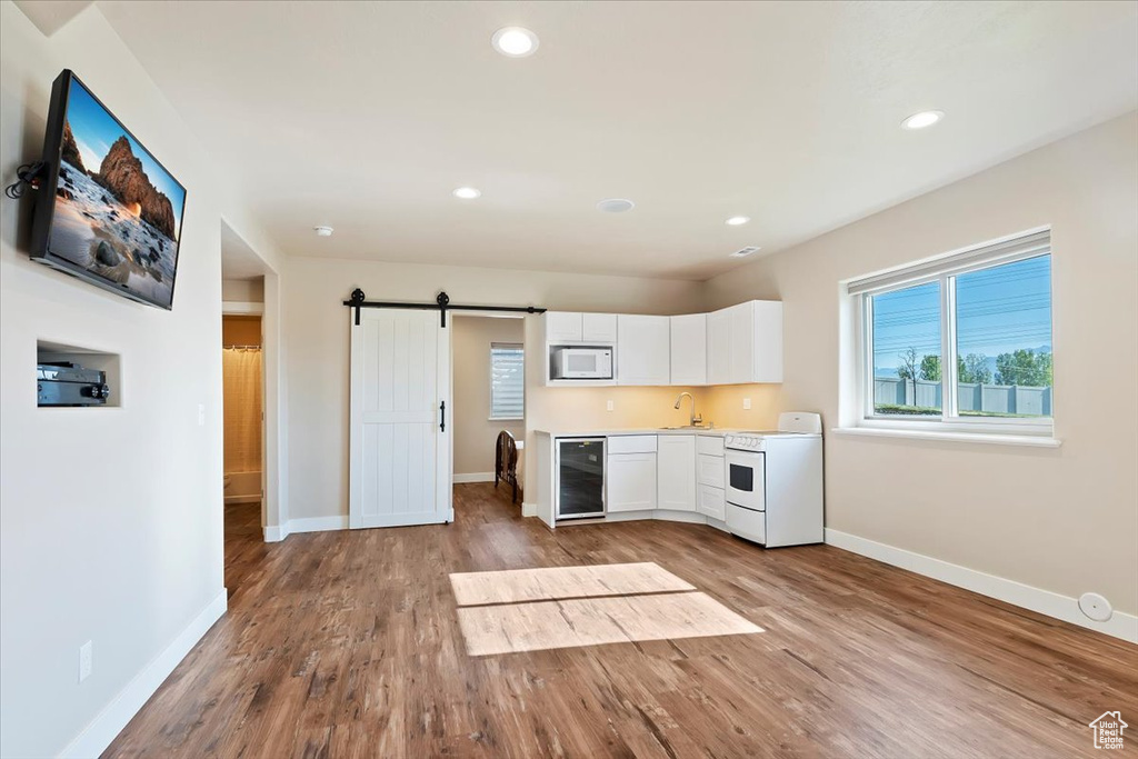 Kitchen with stove, wood finished floors, baseboards, white microwave, and wine cooler