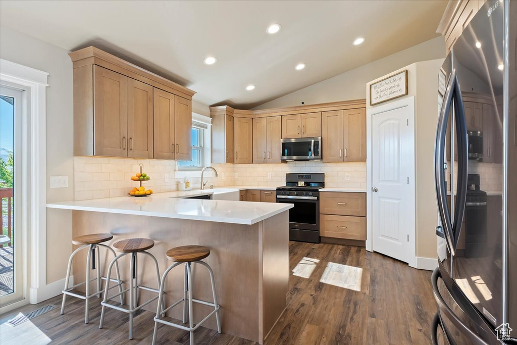 Kitchen with appliances with stainless steel finishes, vaulted ceiling, a peninsula, and dark wood-type flooring