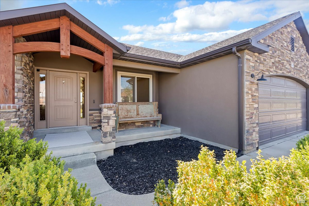 Property entrance with a garage, stone siding, and stucco siding