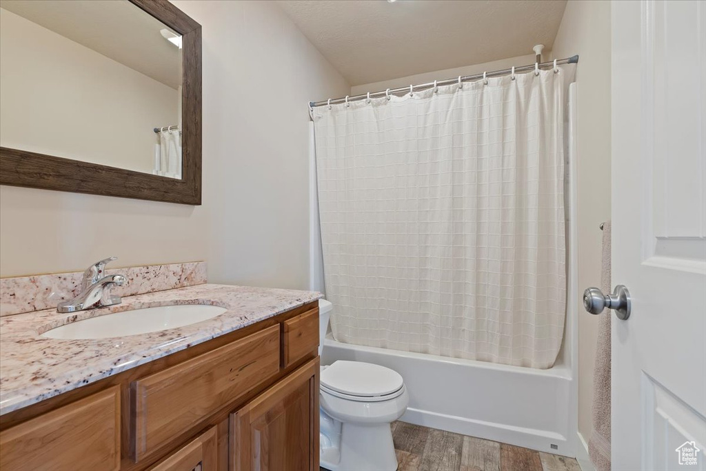 Bathroom with toilet, shower / bathtub combination with curtain, wood finished floors, and vanity