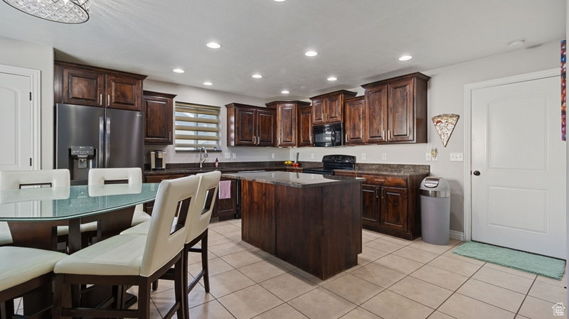 Kitchen featuring dark countertops, black microwave, stainless steel fridge, dark brown cabinetry, and range with electric cooktop