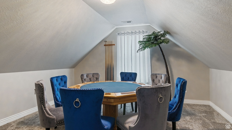 Carpeted dining area featuring baseboards, vaulted ceiling, a textured ceiling, and visible vents