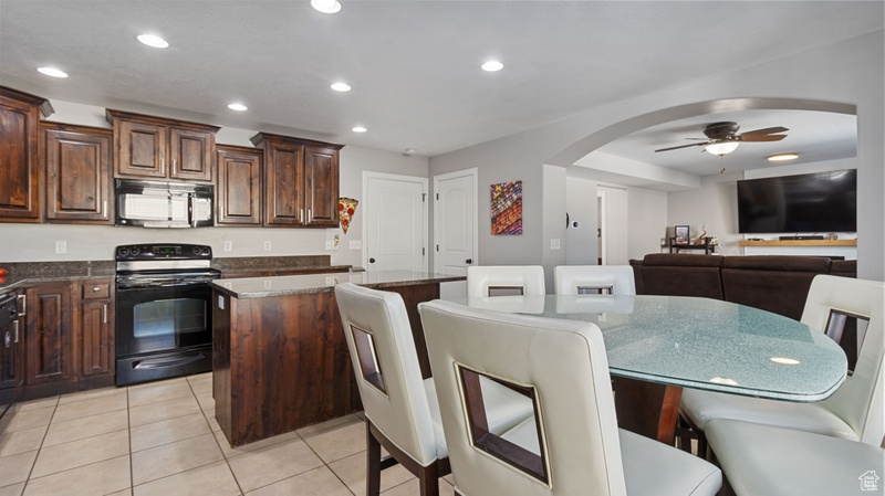 Kitchen featuring black range with electric cooktop, a kitchen island, ceiling fan, recessed lighting, and arched walkways